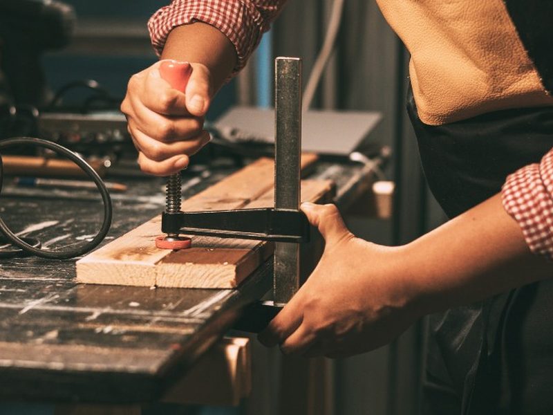 Carpintero apretando un sargento para encolar dos piezas de madera en el banco del taller